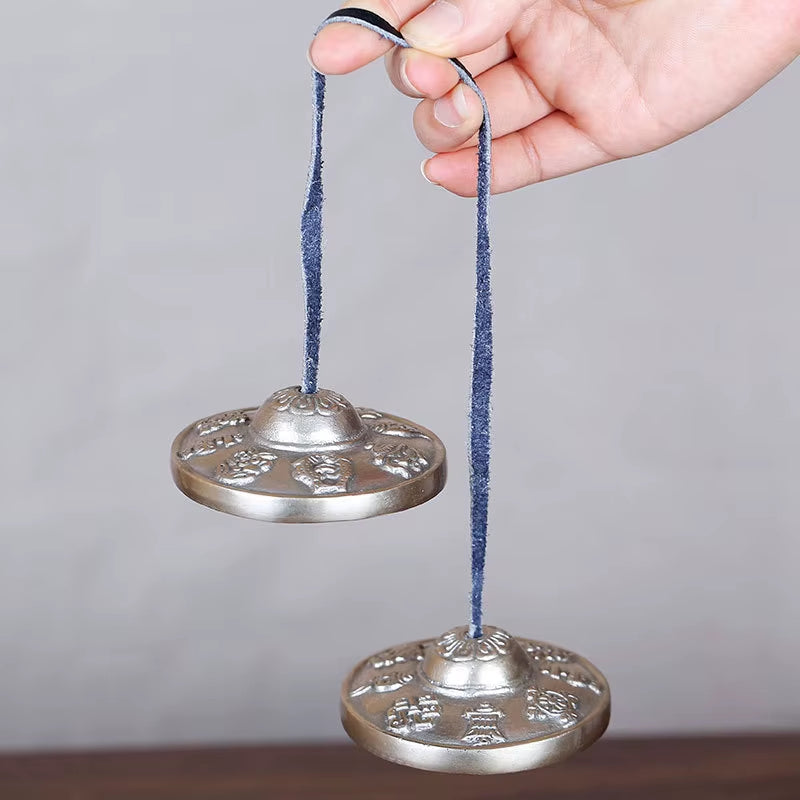 Two silver Tibetan tingsha cymbals with blue cords for meditation and yoga