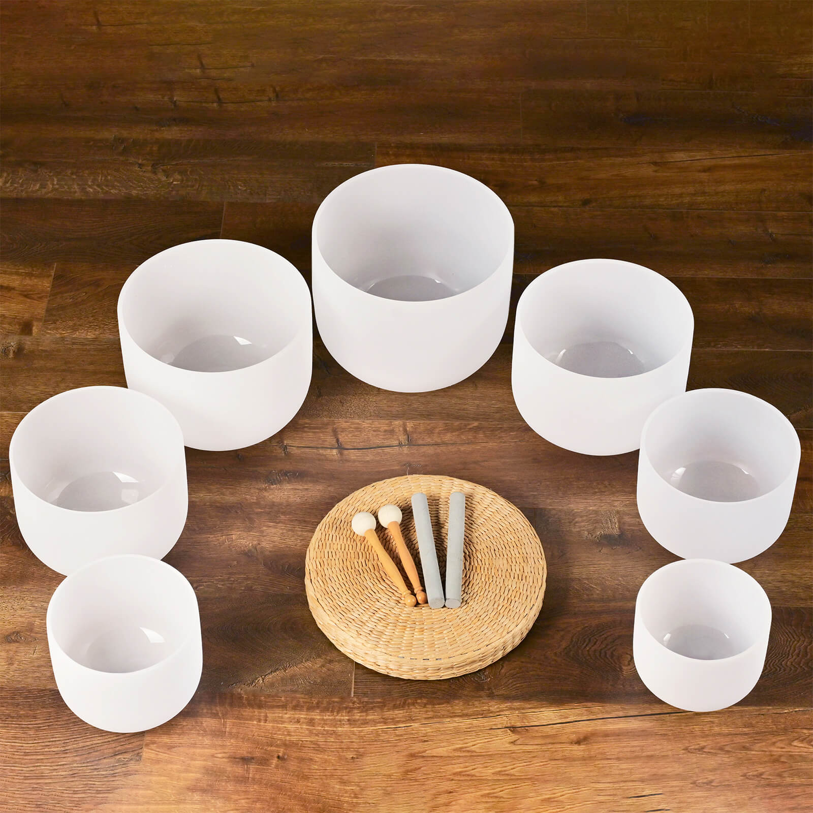 Seven white crystal singing bowls in a semicircle on a woven mat with mallets